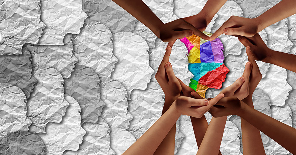Crinkled up paper in the shapes of many side profile heads in white with one side profile in many colors with hands around it in the shape of a heart