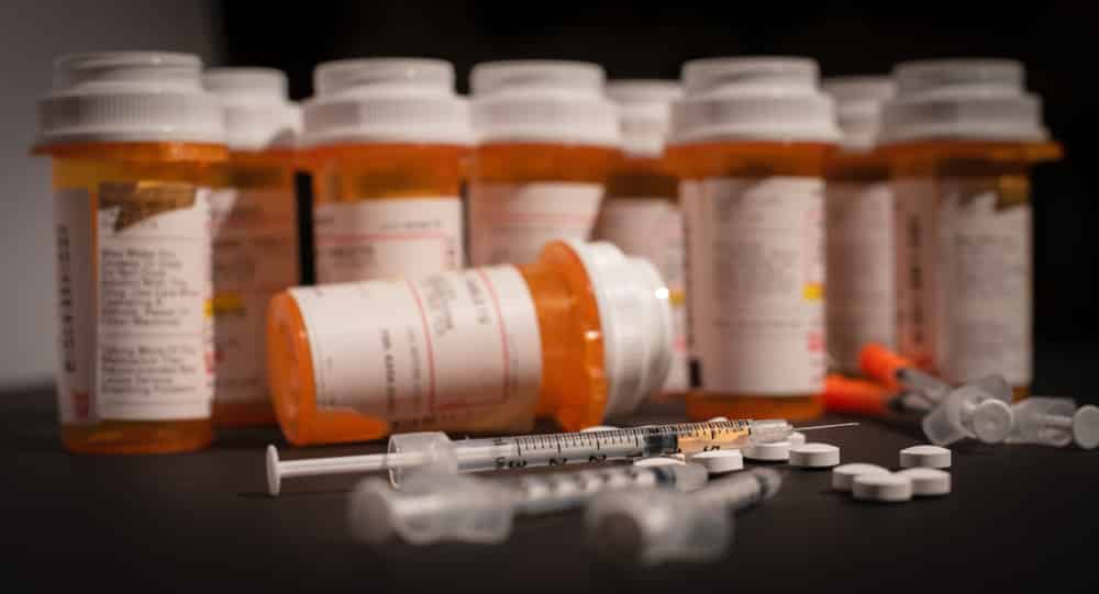Prescriptions medication bottles lined up in the background of pills, tablets and syringes representing overdose awareness day.