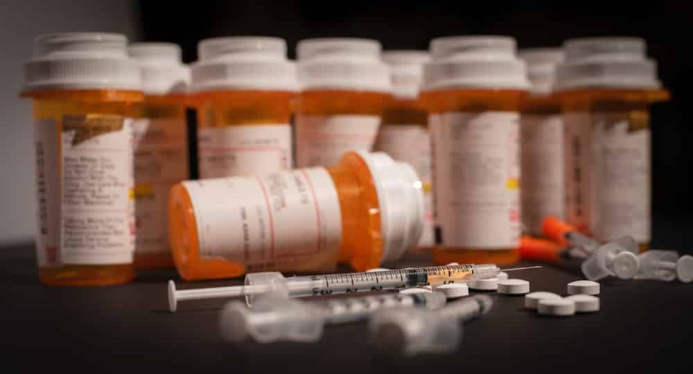 Prescriptions medication bottles lined up in the background of pills, tablets and syringes representing overdose awareness day. 