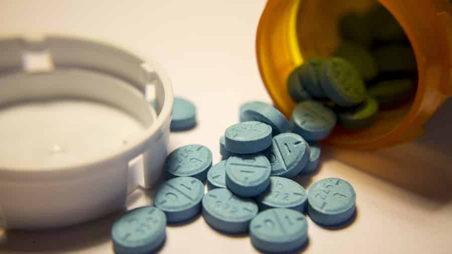 A prescription bottle is spilled over with blue Adderall pills laid out representing the signs of addiction and how to recover. 
