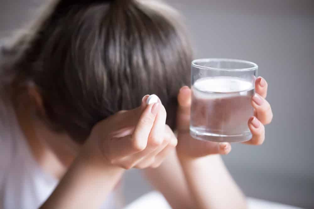 Girl with face down, hair in ponytail with head resting on hands holding water and a pill