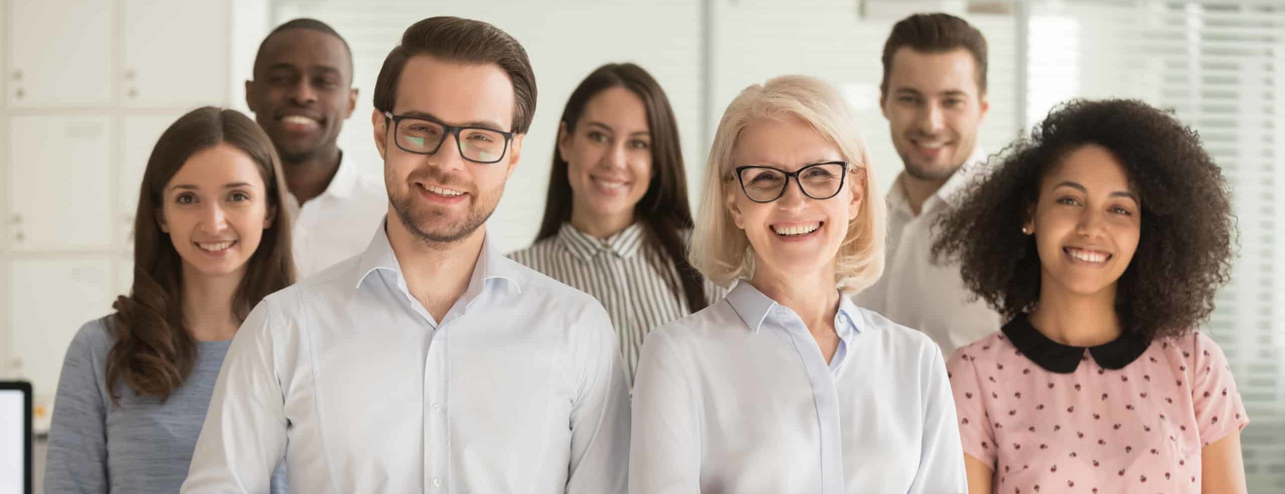 Several adults from varying backgrounds looking straight, smiling, dressed professionally in bright lit room