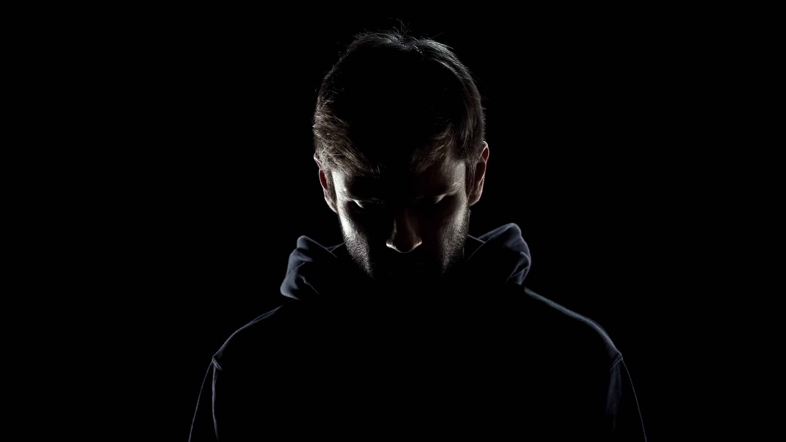 Dark filtered black wall with dark profile of man in hoodie staring down