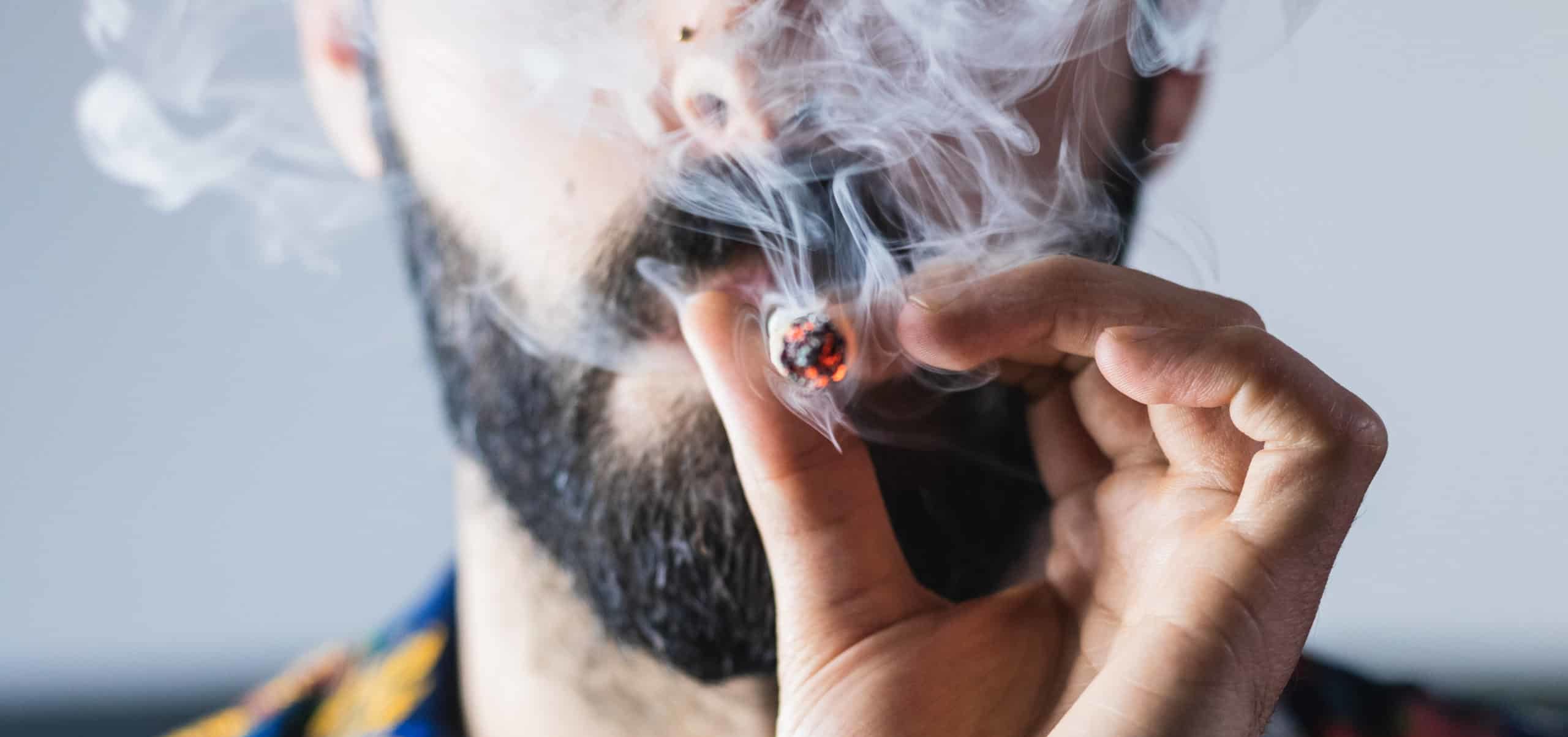 Close up of man with beard and mustache smoking marijuana joint