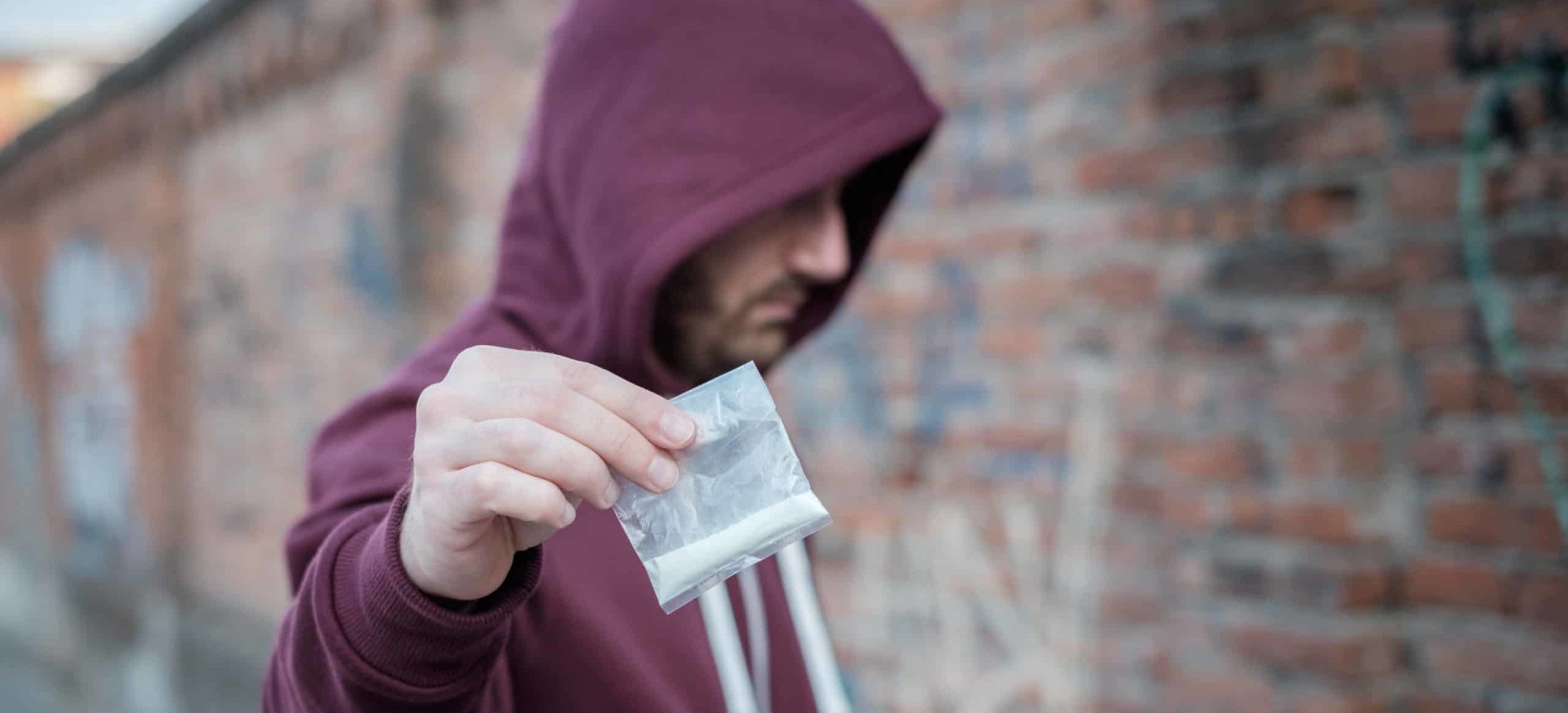 Out of focus man in need of meth addiction treatment, holding up a bag of white powdery meth