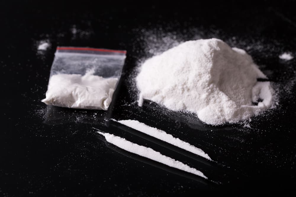  White fine powdered cocaine in a pile, in a bag, and in two lines on top of black table