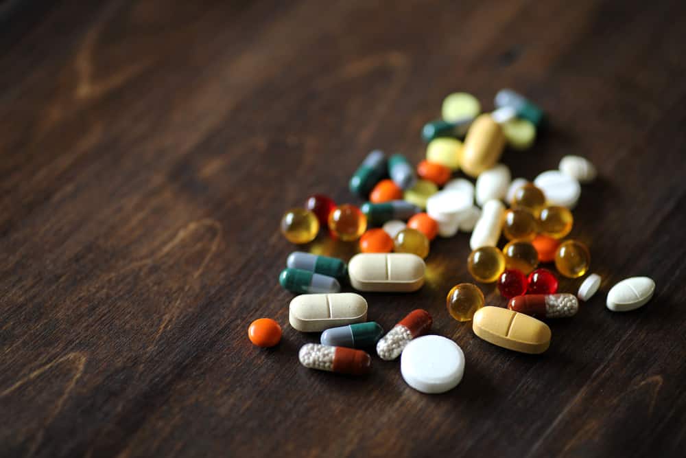 Many, various pills laying in a pile together on a wooden table