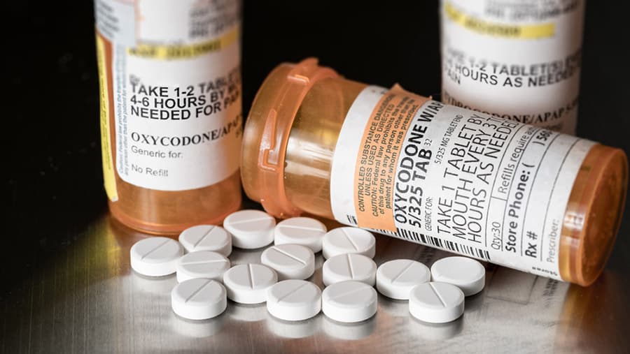 Three prescription medication bottles with white oxycodone pills spilling out of one bottle to help with safe and successful opiate withdrawal.