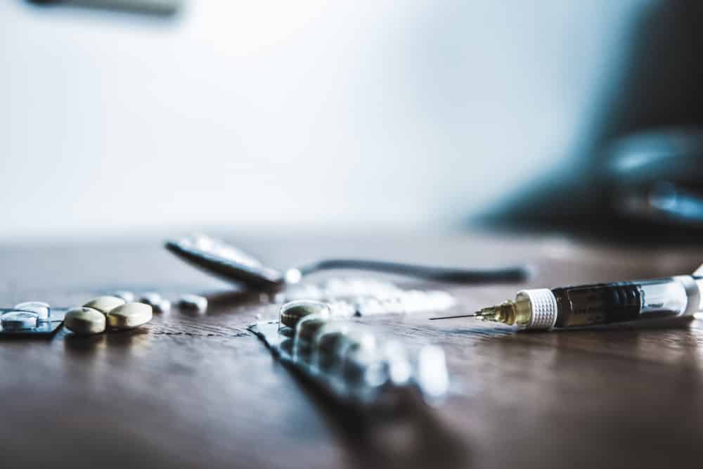 Wood table with pills, spoon, white powder fentanyl, and full syringe laying on it