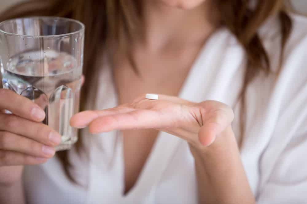 neck and shoulders of woman, who needs oxycodone addiction treatment, holding up pill with glass of water