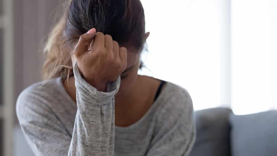 A stressful looking female suffering from addiction and trauma has her head in her hand. 