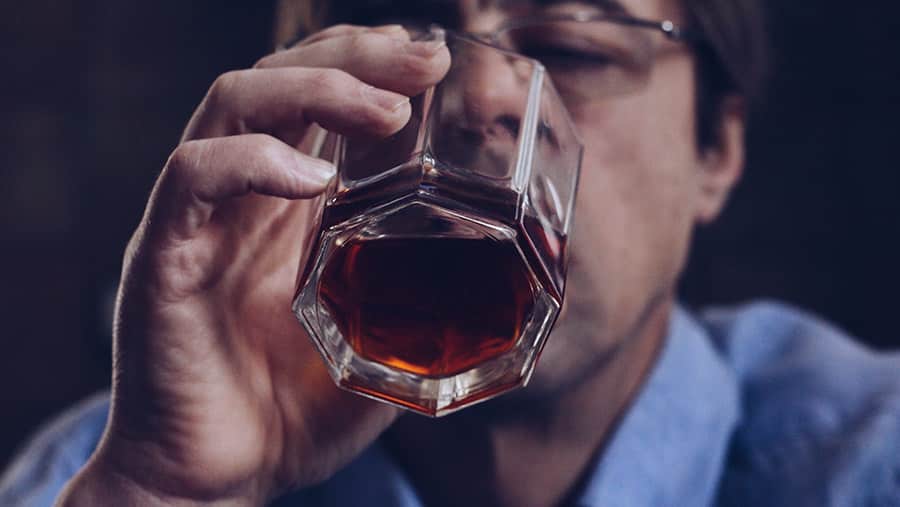 A man with glasses is actively drinking a glass a cup of alcohol after just having gotten the covid vaccine. 