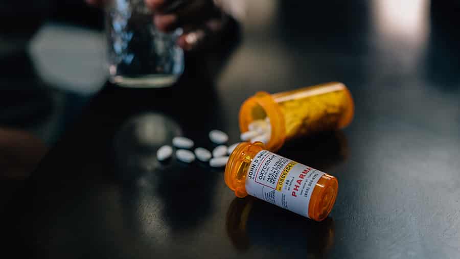 Two prescription opioid bottles with white pills spilling out onto a dark table represent the signs of drug and opioid addiction.