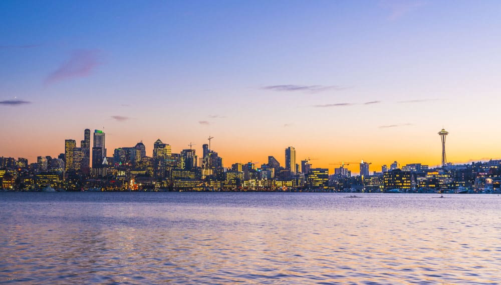 Cityscape of Seattle with blue and golden sun setting sky, high rise buildings profiles, and water