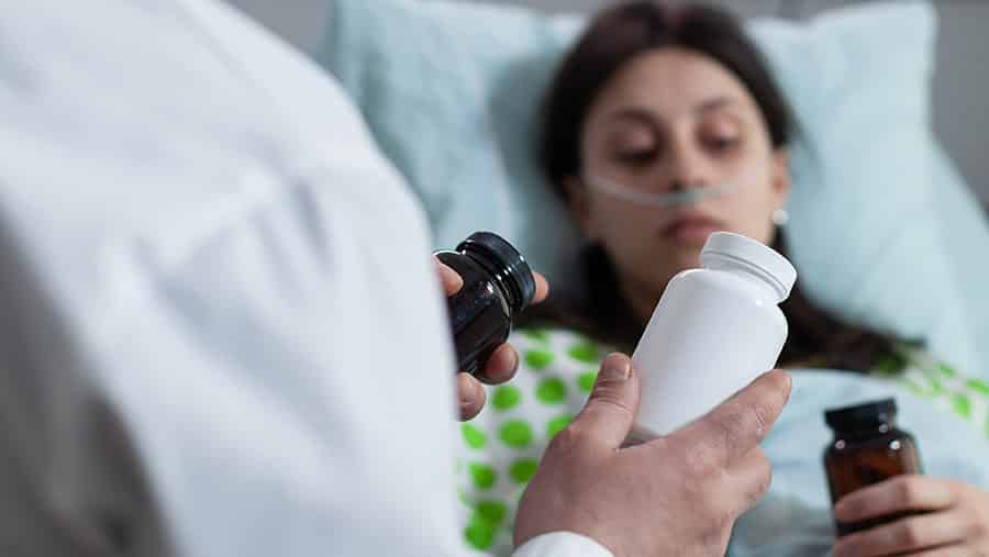 A medical professional explains to a woman laying in a hospital bed the suboxone withdrawal process, symptoms and timeline, while holding prescription medication bottles. 