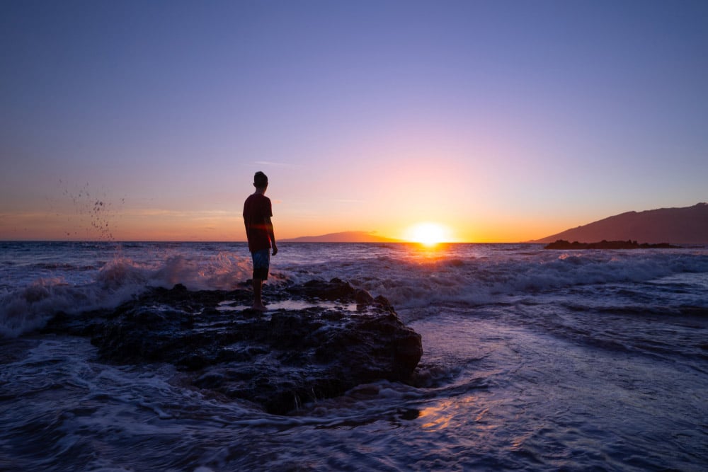 Hopeful man staring at sunset with feet in the ocean