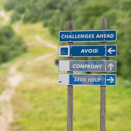 Stacked navigation signs with arrows going in different directions - outdoors with roads, saying "challenges ahead", "avoid", "confront", "seek help"
