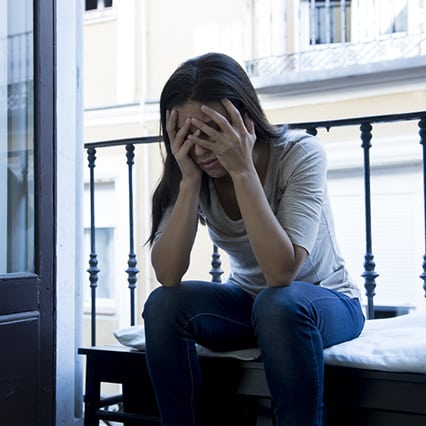 Woman sitting on a bench on a porch with head in hands, visibly upset
