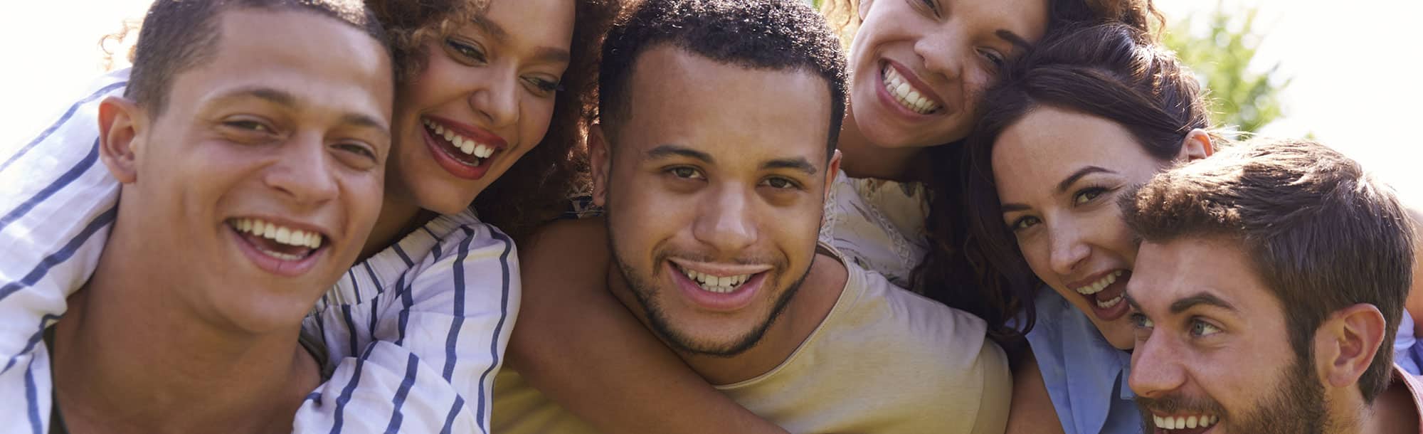Men and women's faces close to one another in group hug, all smiling and happy