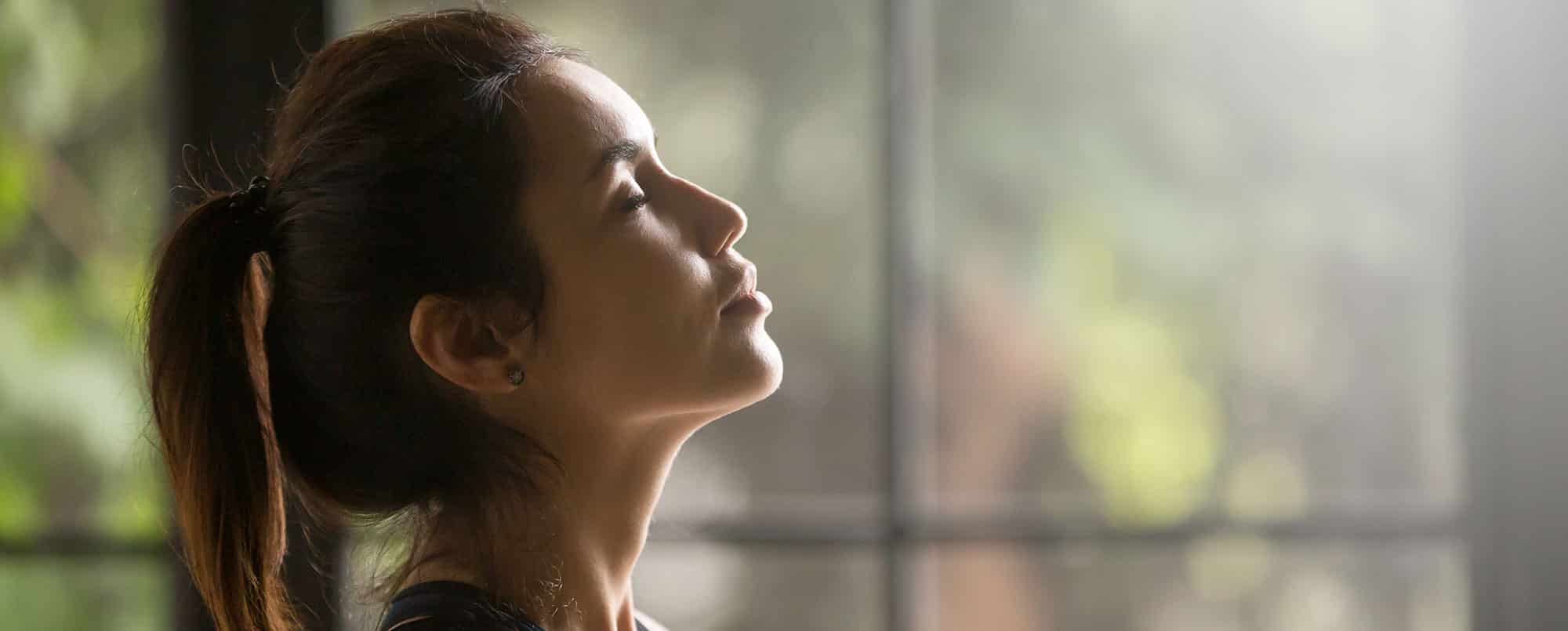 Profile of brown haired woman closing her eyes and putting face towards the sky