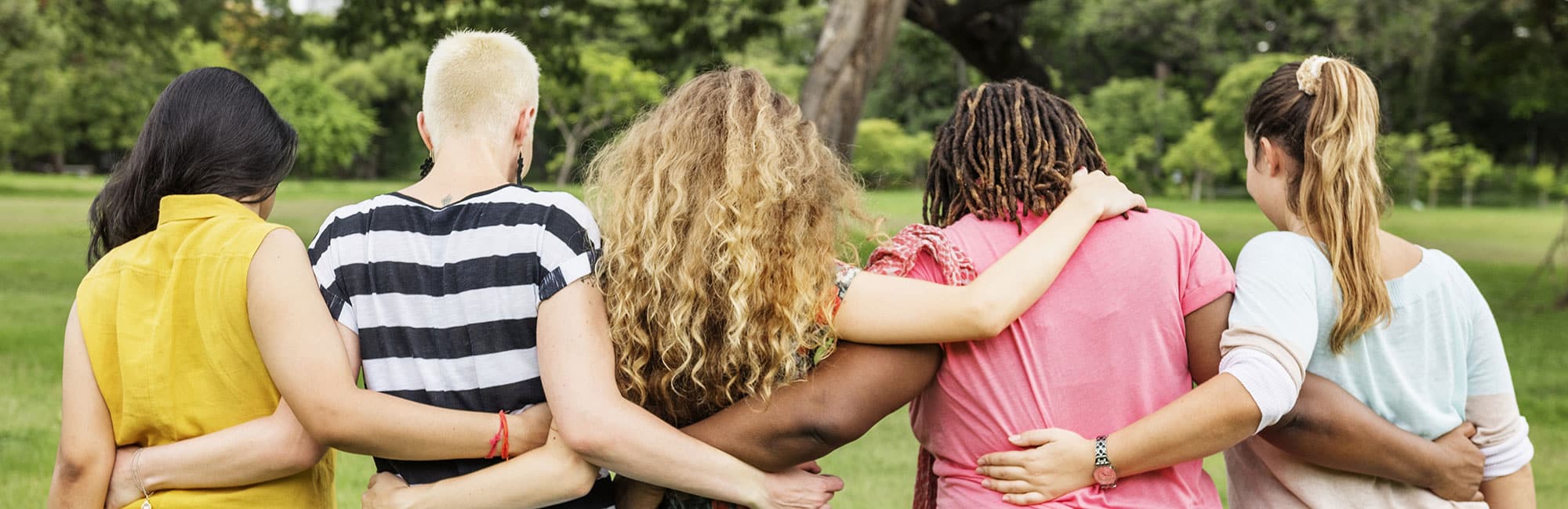 the backs of five women, brightly dressed, supporting each other in a drug and alcohol rehab for women