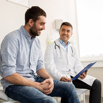 Large man smiling and sitting next to Doctor looking at clipboard