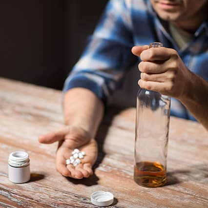 Man with substance use disorder sits at table with whiskey glass and a hand full of pills