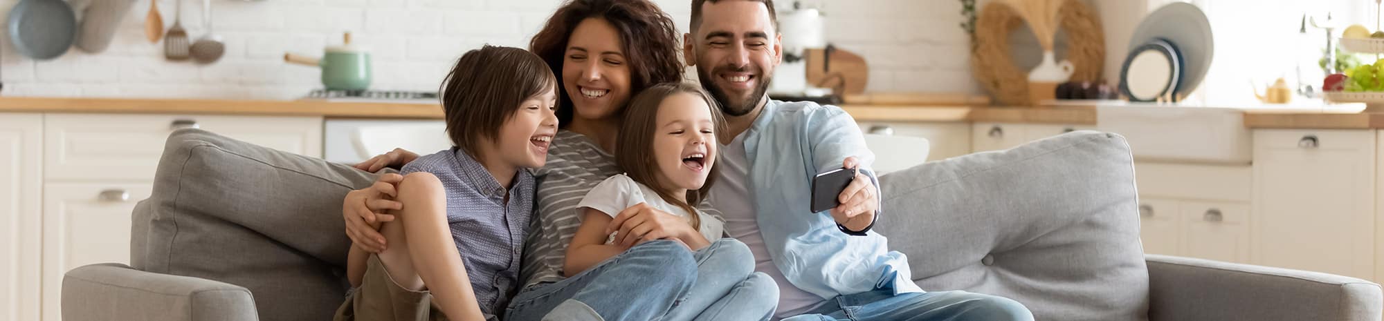Mom, dad, and two kids reunited after a family addiction program - sitting on a couch and smiling while watching dads cellphone