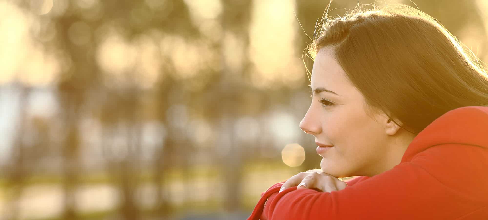 Side profile of young brunette girl wearing orange hoodie, content sitting outside