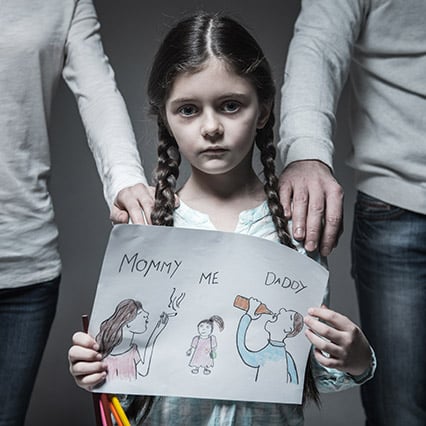 Sad little girl standing in the middle of her parents holding a drawing of her mom smoking and dad drinking, each one has a hand on her shoulder