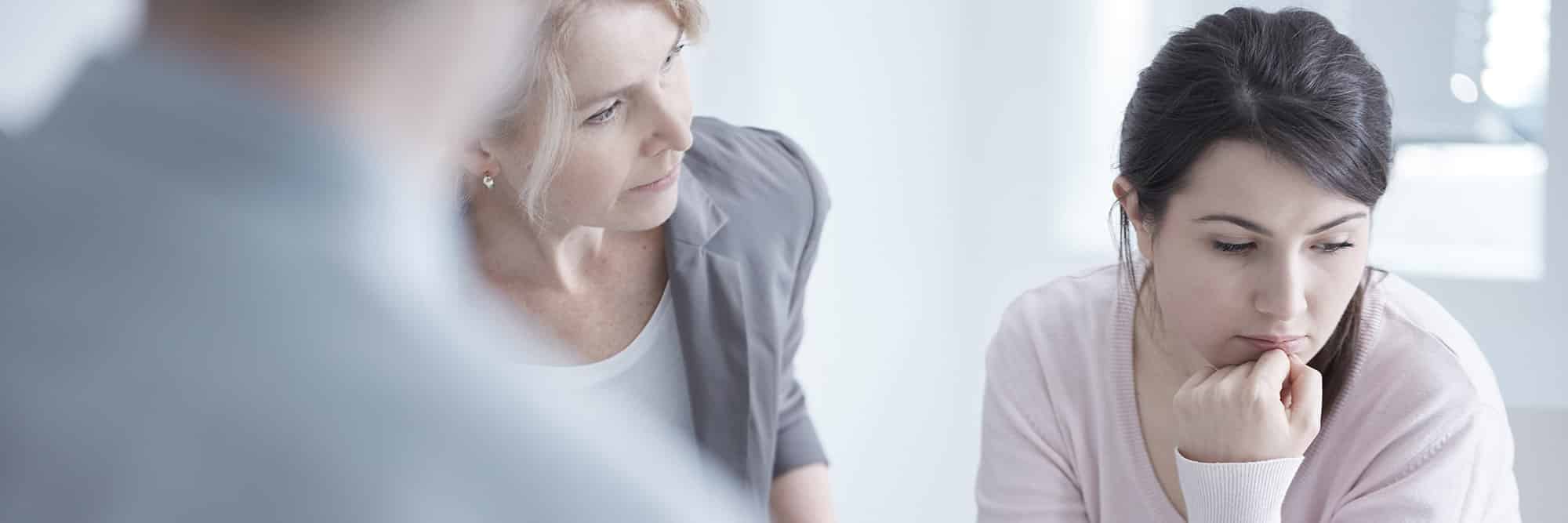 woman looking away with head on hand as other older woman looks at her in an accusatory way