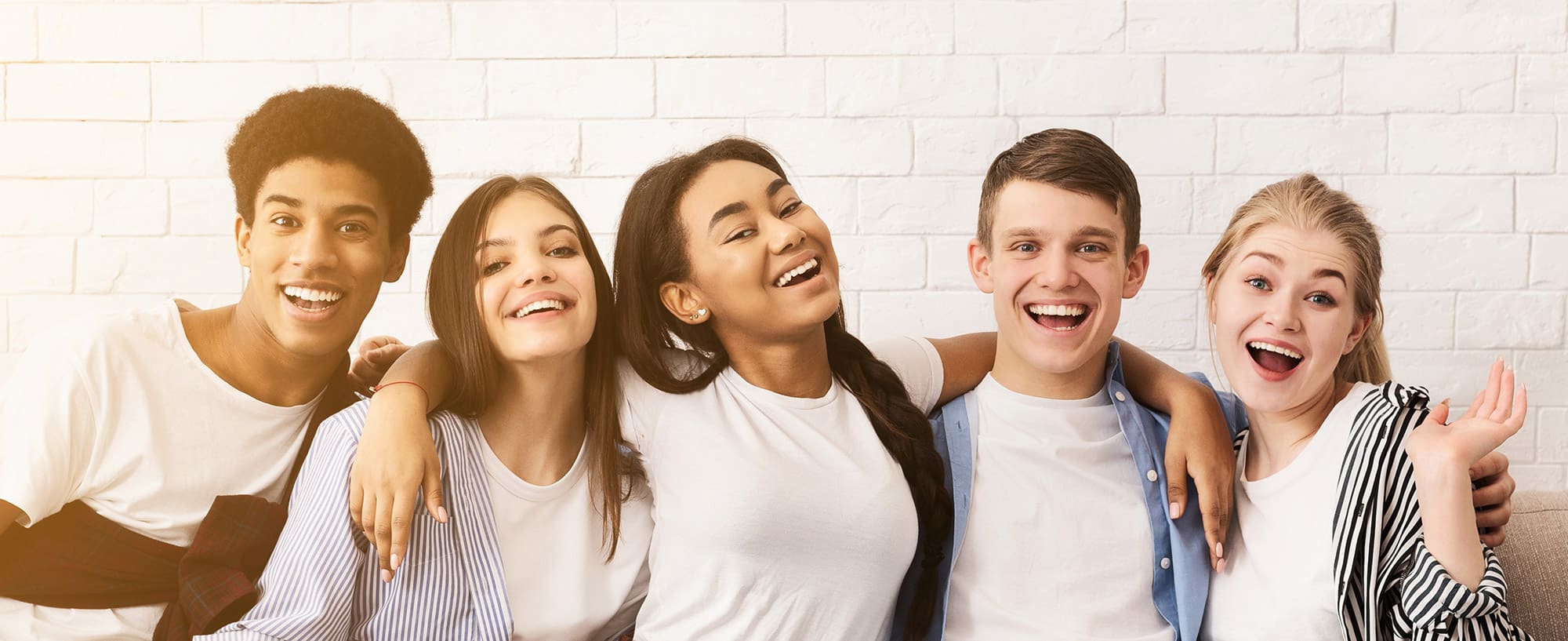 five happy young adults at drug and alcohol rehab, standing in front of brick wall