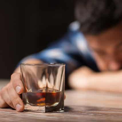 off-focus man with alcoholism reaching for glass of whiskey