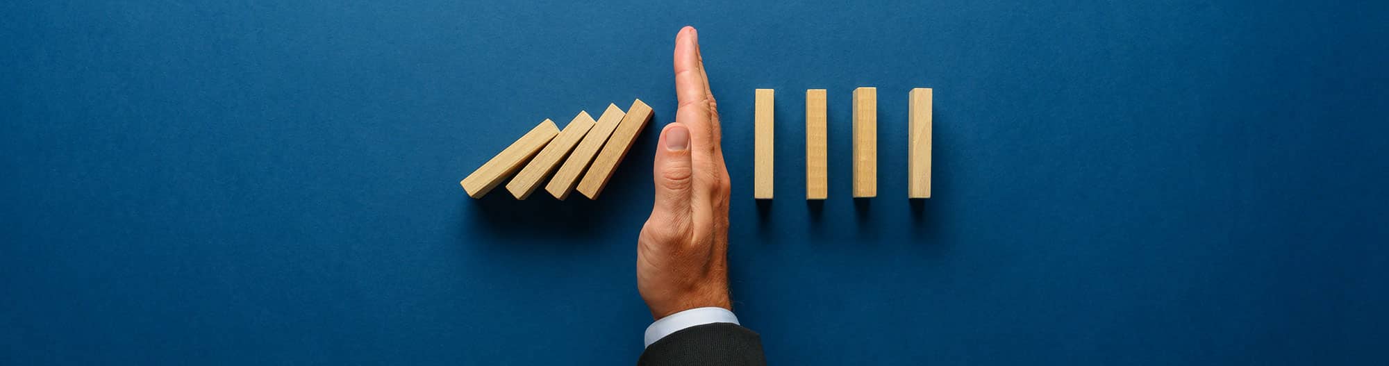 Manly hand in suit stopping domino effect from hitting wood blocks