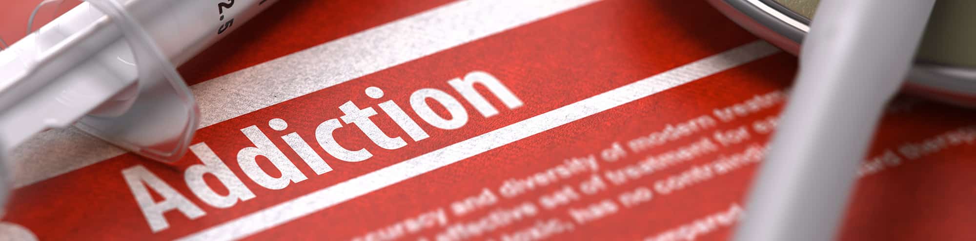Addiction typed on note pad in red and white with syringes in background 