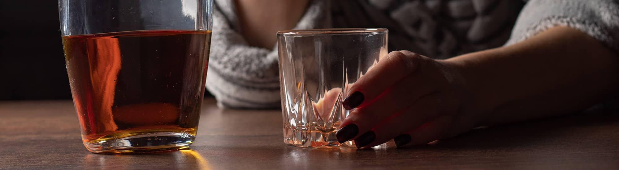 Woman's hand with painted fingernails holding empty whiskey glass near whiskey bottle 