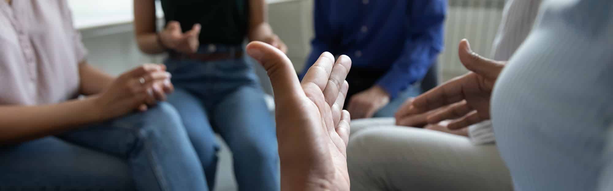 Five people in group therapy at an inpatient drug rehab, sitting in a circle with expressive hands
