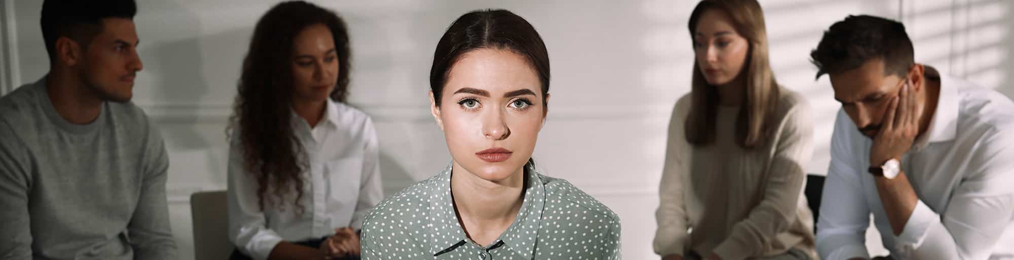 Serious woman staring straight with five people sitting in a circle behind looking confused and stern