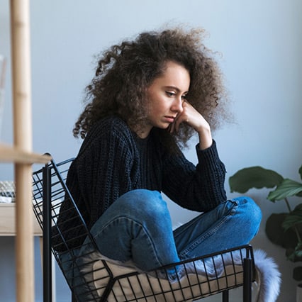 Girl sitting cross legged in chair, with face leaning on arm contemplating if she needs inpatient drug rehab ohio