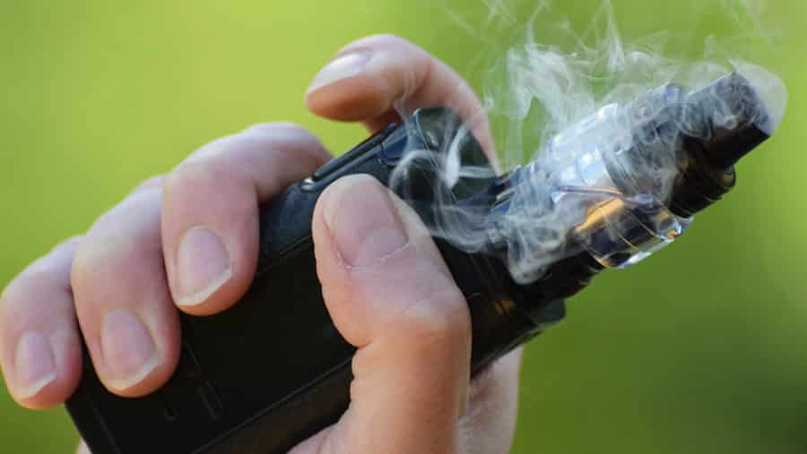 A person is holding a black handheld vape device surrounded by smoking vapors. 