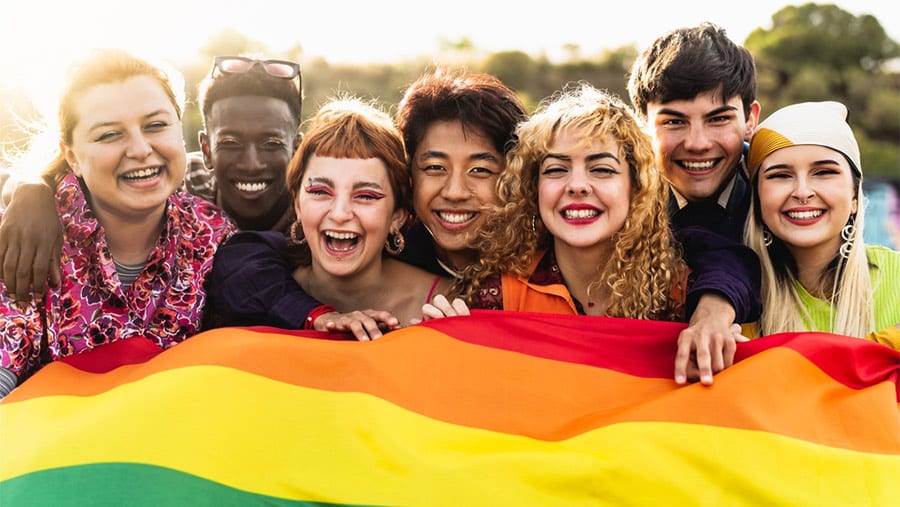 A group of multiracial adults with substance use disorders and co-occurring mental health conditions holding a rainbow flag to represent the LGBTQIA+ community