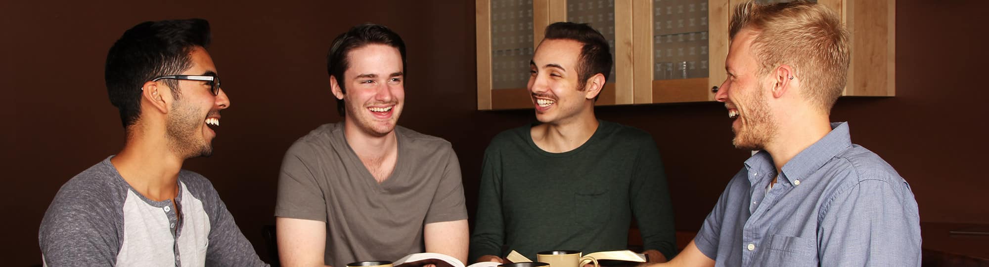 Four men in modern clothing, sitting at a table and smiling, laughing together