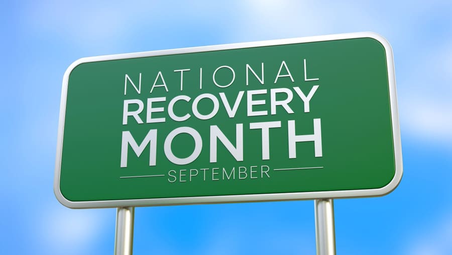 A green U.S. highway sign says National Recovery Month September written in white letters. 