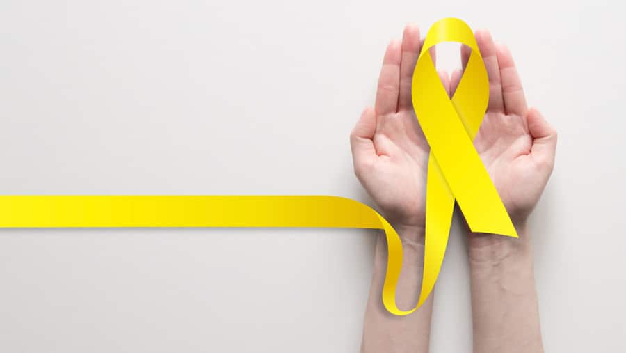 A person’s hands are holding a yellow ribbon representing the Suicide & Crisis Lifeline 988 as an alternative to 911 for mental health emergencies. 