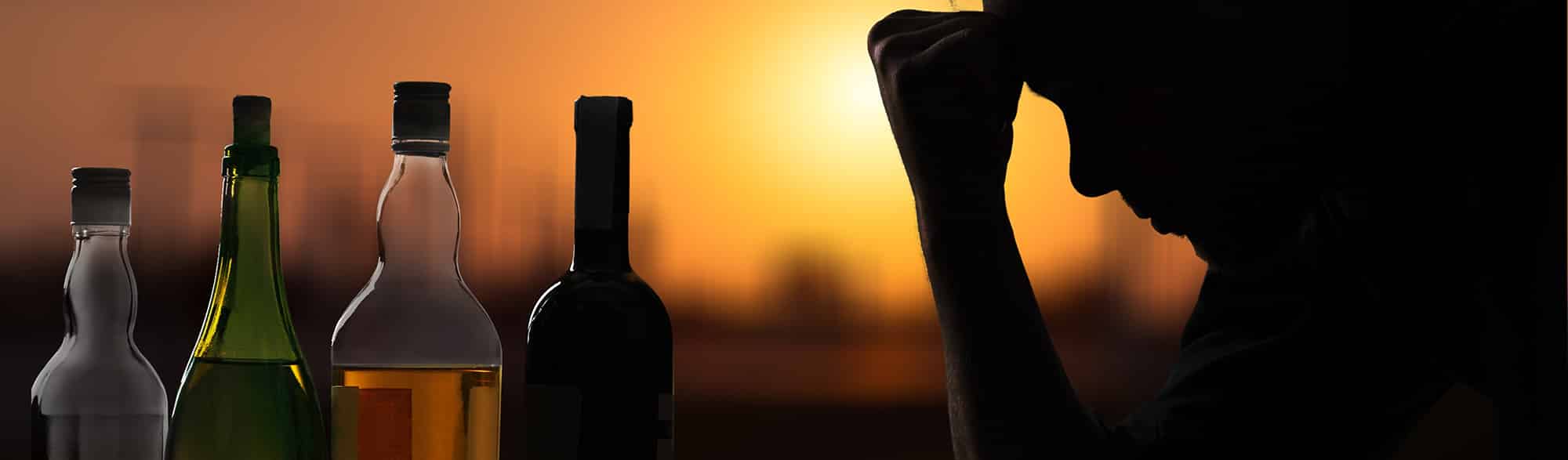 Black profile of mans head looking down, resting on hand with the tops of many bottles of liquor