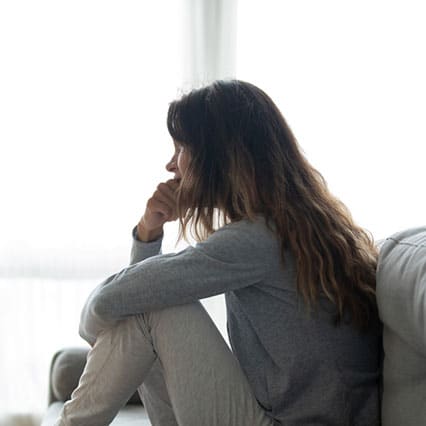 side profile of woman sitting scrunched up on a couch, in need of rehab, biting her nails
