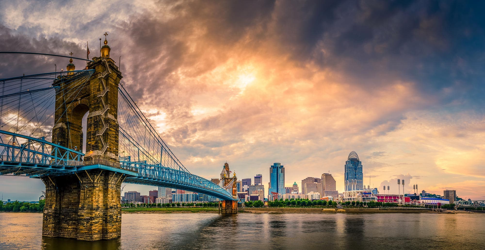 Cincinnati Bridge sprawling over Ohio river into Cincinnati City Scape with beautiful golden clouded skies with Hotel California by the Sea logo