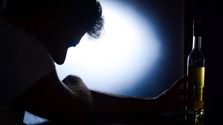 A dark silhouette of a person experiencing alcohol delirium tremens is hunched over holding a bottle of wine. 