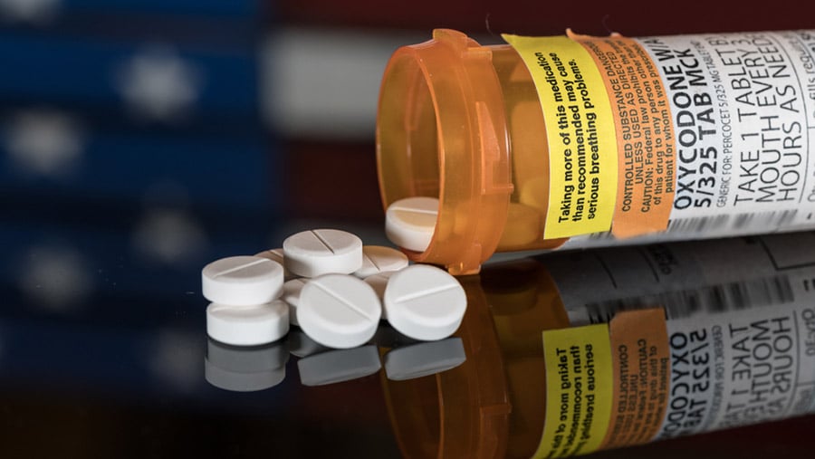 A prescription pill bottle spilling over white tablets represents possible symptoms of oxycodone overdose. 