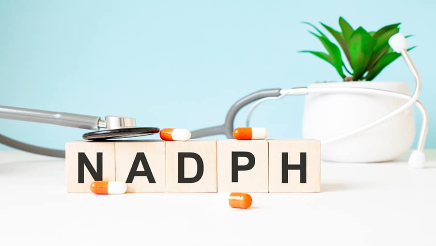 Blocks of letters spelling out NADPH next to orange pills and a stethoscope represents NAD treatment for addiction.